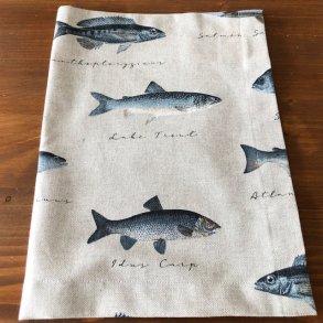 Dkkeservtiet i beige/ lyst stof med motiver af forskellige fisk.