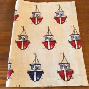 Dkkeservtiet i beige/ lyst stof med motiver af fiskekuttere.