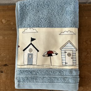G�steh�ndkl�de i lys bl� med en bort af farvestr�lende badehuse forneden.
