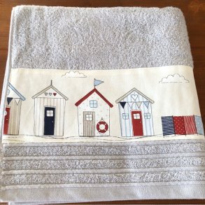 Badehndklde i lys gr farve med en bort med badehuse forneden.