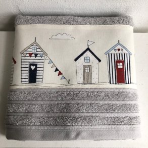 Hndklde i lys gr med en bort af sm farvestrlende badehuse forneden.