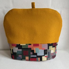 Tehtte i karrygul uld med kant af farvestrlende gobelin forneden.