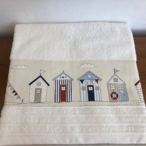 Badehndklde i cream med en bort af forskellige badehuse forneden.